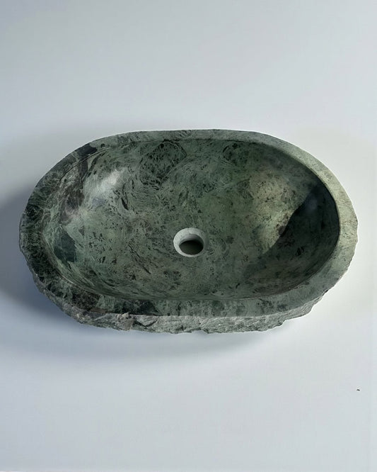 Handcrafted green natural stone oval vessel sink with dark mineral veining, carved basin interior, and rugged textured edges on a white background.